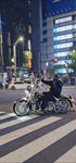 Person riding a motorcycle on a city street at night with illuminated signs and lights.