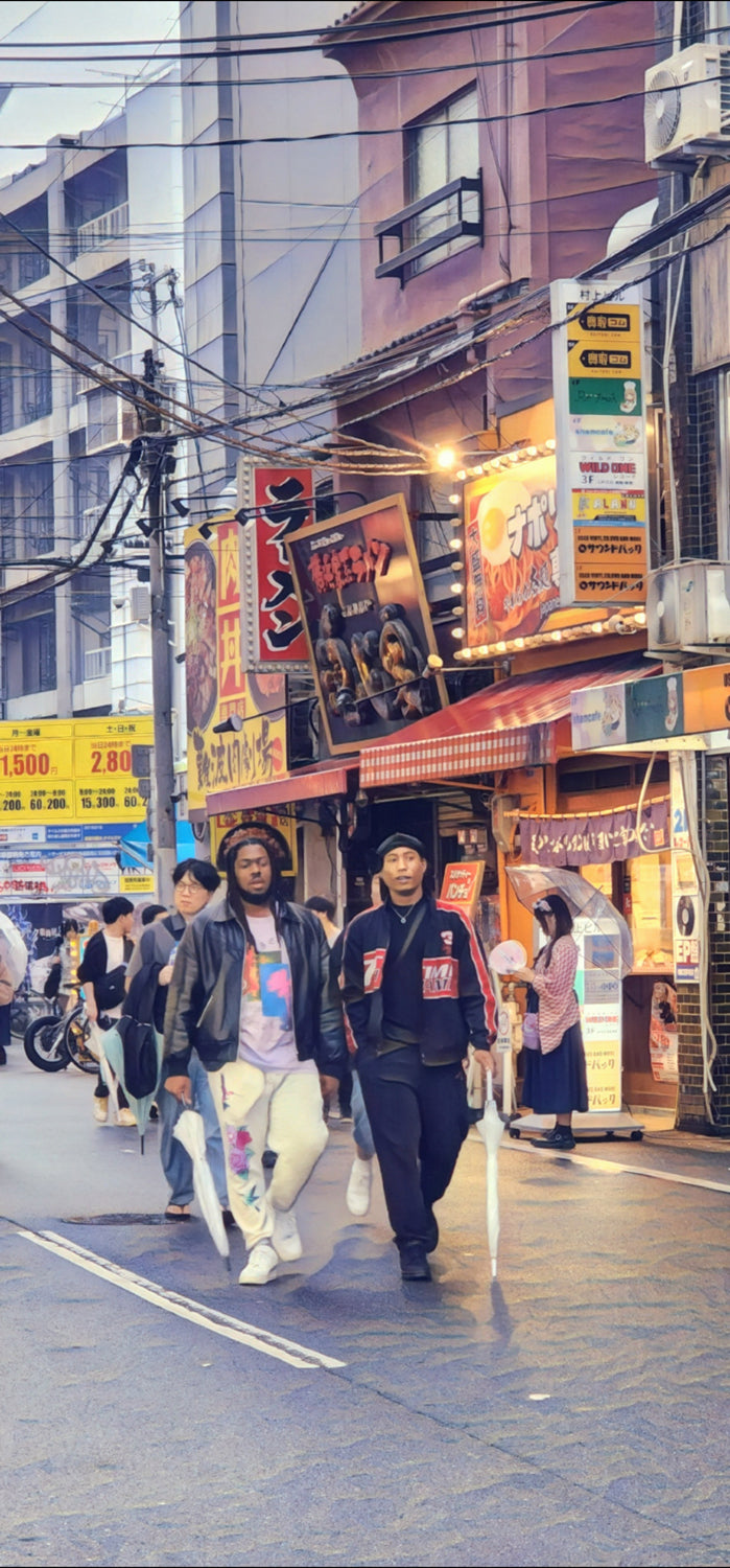 Evening street in Japan with ramen shop signs and three people walking with clear umbrellas on a wet road.