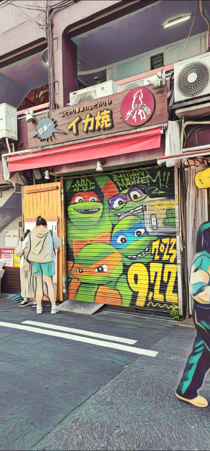 Painted shutter showing cartoon turtle faces and a boombox at a Japanese shopfront; red awning and pedestrians